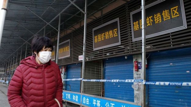 Pedestre com máscara passa ao lado de mercado popular com lojas fechadas